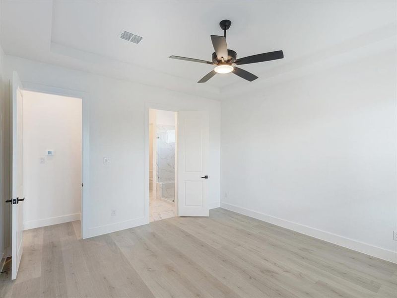 Primary bedroom featuring light wood-style floors, ceiling fan, and ensuite bath Primary bedroom featuring light wood-style floors, ceiling fan, and ensuite bath