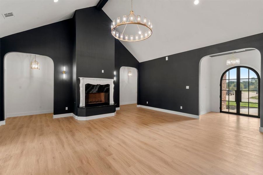 Unfurnished living room featuring a chandelier, arched walkways, high vaulted ceiling, light wood-style flooring, and a premium fireplace
