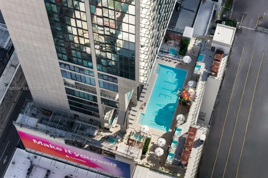 Aerial perspective of high-rise structure featuring an outdoor swimming pool, paved sundeck, elevated terrace space, and glass-facade exterior