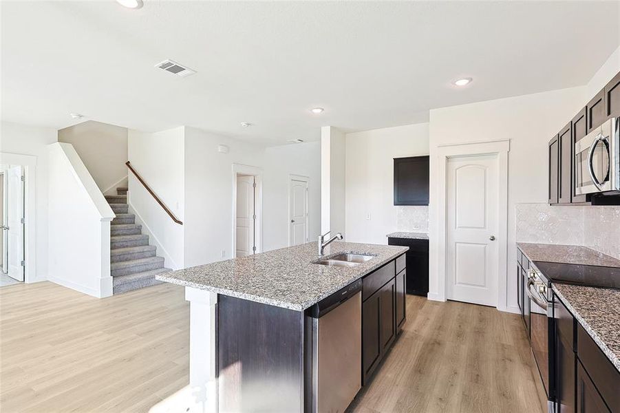 Kitchen featuring an island with sink, sink, tasteful backsplash, light hardwood / wood-style flooring, and appliances with stainless steel finishes