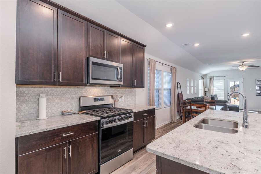 Kitchen featuring light stone counters, stainless steel appliances, a sink, vaulted ceiling, and open floor plan