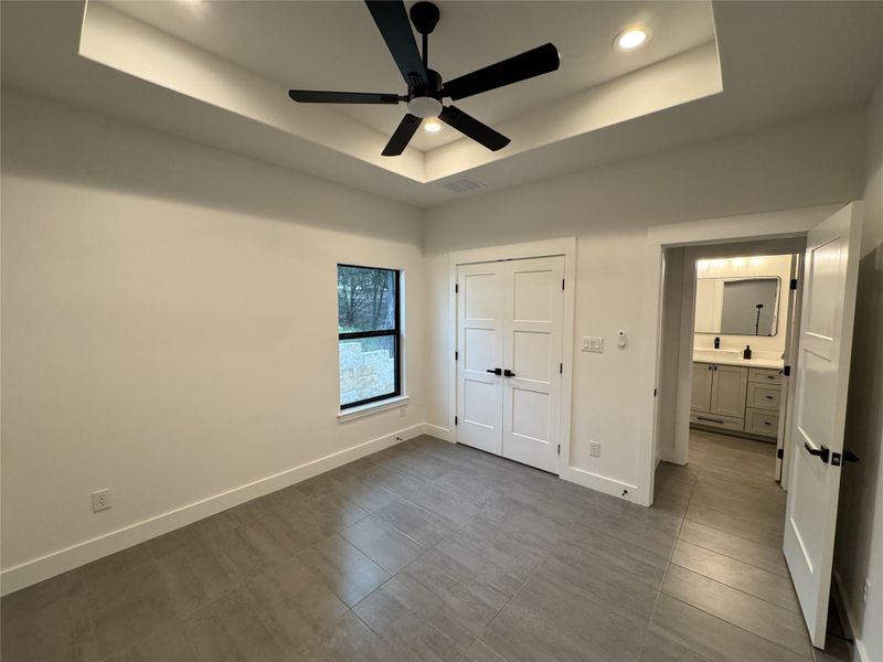 Unfurnished bedroom with a tray ceiling, recessed lighting, dark tile patterned flooring, and ceiling fan Unfurnished bedroom with a tray ceiling, recessed lighting, dark tile patterned flooring, and ceiling fan