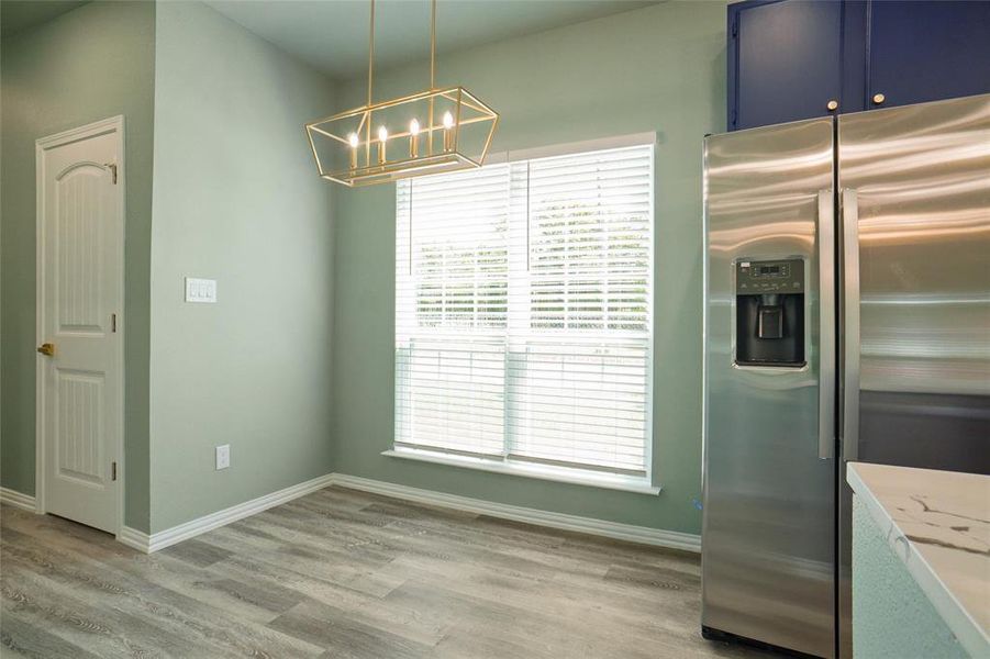 Kitchen featuring stainless steel fridge, light stone countertops, blue cabinetry, decorative light fixtures, and light hardwood / wood-style floors