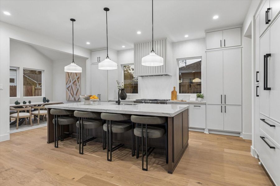 A large quartzite island with a breakfast bar is complemented by stylish milk glass pendant lights, creating the perfect spot for casual dining.