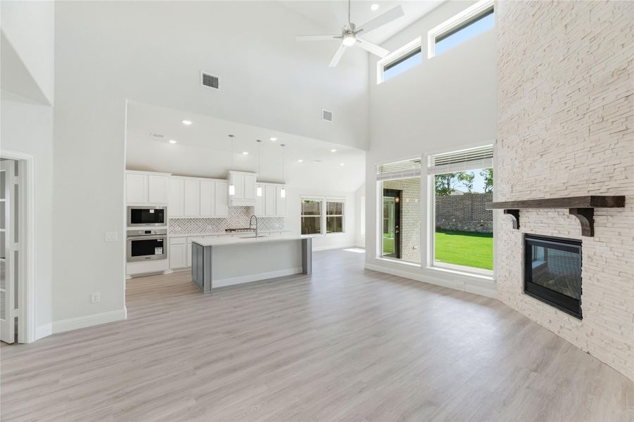Open-concept living area with vaulted ceiling, stone fireplace, and kitchen with large island and white cabinets