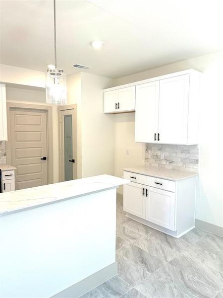 Kitchen with white cabinets, tasteful backsplash, decorative light fixtures, and light stone countertops