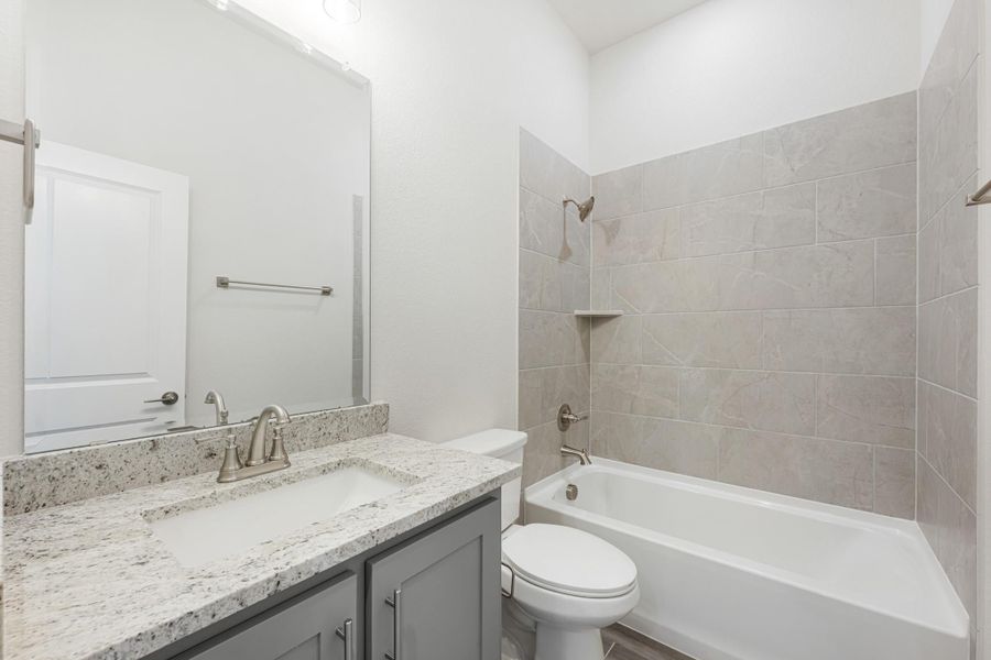 Bathroom with gray vanity, granite countertop, and tiled shower-tub combo with brushed nickel fixtures Bathroom with gray vanity, granite countertop, and tiled shower-tub combo with brushed nickel fixtures