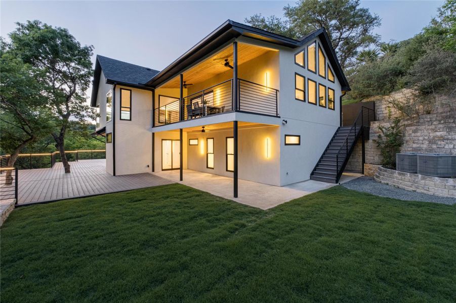 Back of house with a ceiling fan, stucco siding, stairs, a balcony, and a flat back side yard