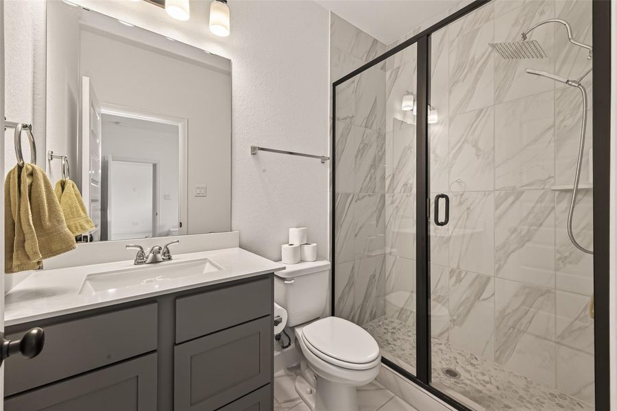This modern bathroom features a sleek vanity with ample storage, a spacious glass-enclosed shower with elegant tilework, and updated fixtures.