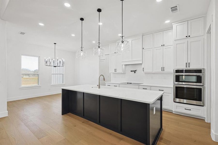 Kitchen featuring decorative light fixtures, sink, a center island with sink, and white cabinets