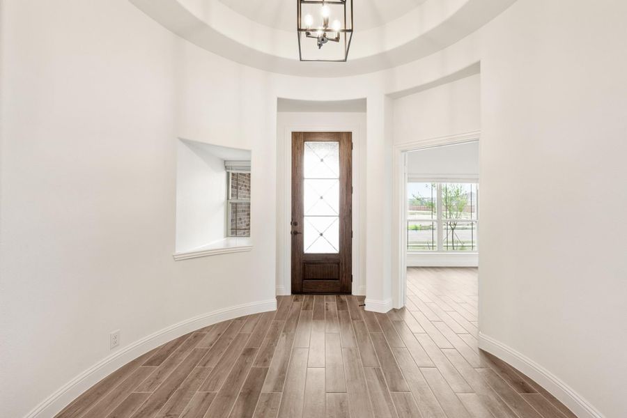 Round foyer with wood front door, tray ceiling, chandelier, and light hardwood floors