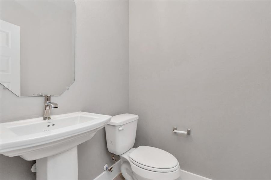 A glimpse of the spacious upgraded half bath featuring a pedestal sink, sophisticated light fixtures, and sleek hardware. Sample photo of completed home with similar floor plan. As-built interior colors and selections may vary.