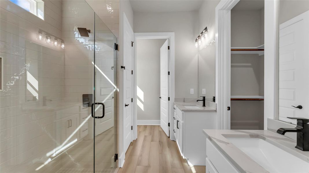 Full bath with two vanities, a stall shower, and light wood-style floors