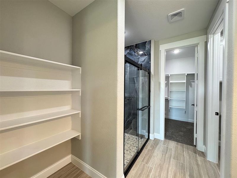 Spacious interior with wood-finish tile flooring, a glass-enclosed shower with dark stone-look wall panels, and an additional walk-in closet featuring built-in shelving