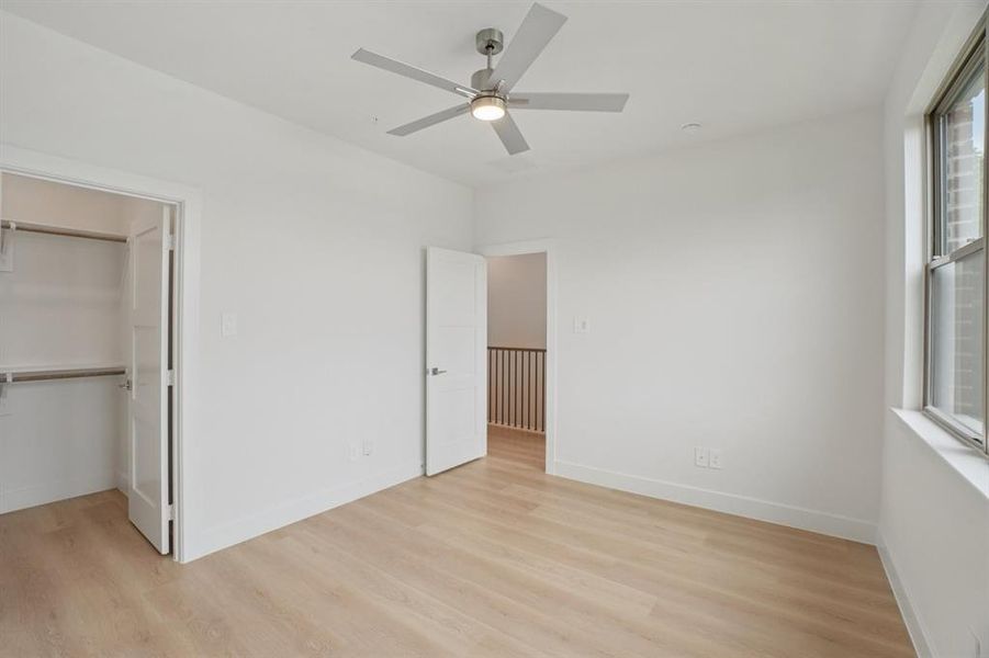 Unfurnished bedroom with light wood finished floors, a spacious closet, and a ceiling fan