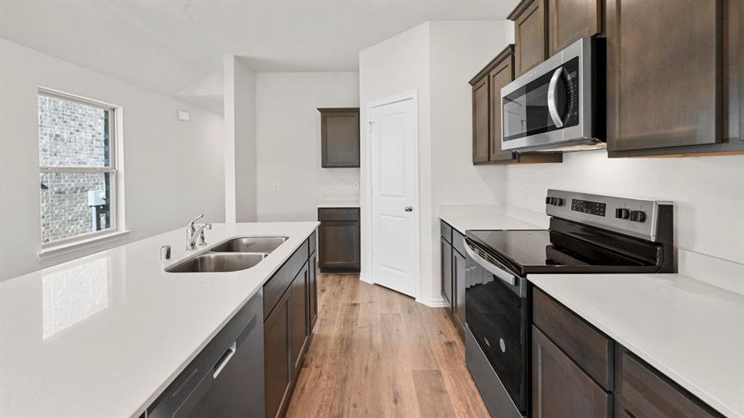 Kitchen with stainless steel appliances, light wood-style flooring, dark wood finish cabinetry, and light stone countertops