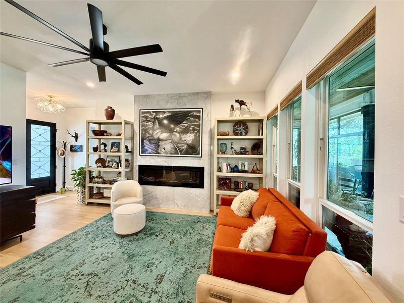 Living area featuring hard-surface flooring, an integrated electric fireplace with a textured accent wall, a multi-blade ceiling fan, recessed lighting, and a series of large windows
