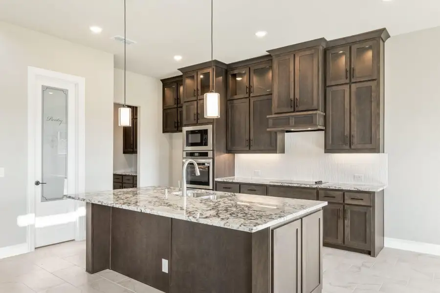 Kitchen with dark wood cabinets, granite island, stainless steel appliances, and pantry door with etched glass
