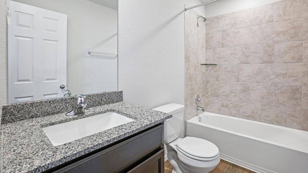 A well-appointed bathroom features a stylish vanity with granite countertops and a tiled shower/tub combo.