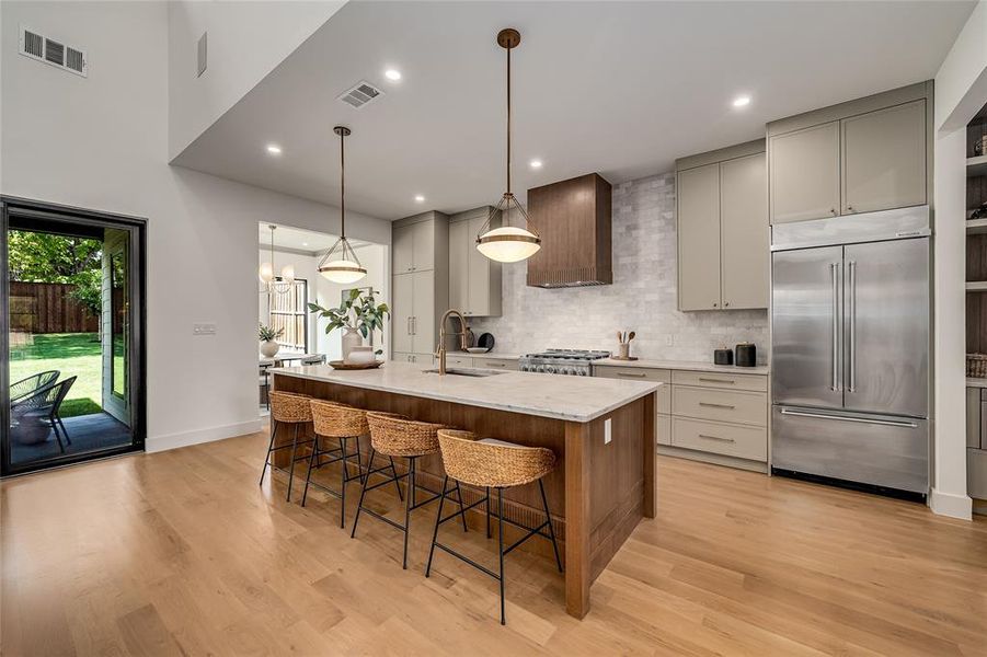 Kitchen with backsplash, appliances with stainless steel finishes, a center island with sink, hanging light fixtures, and light stone counters Kitchen with backsplash, appliances with stainless steel finishes, a center island with sink, hanging light fixtures, and light stone counters