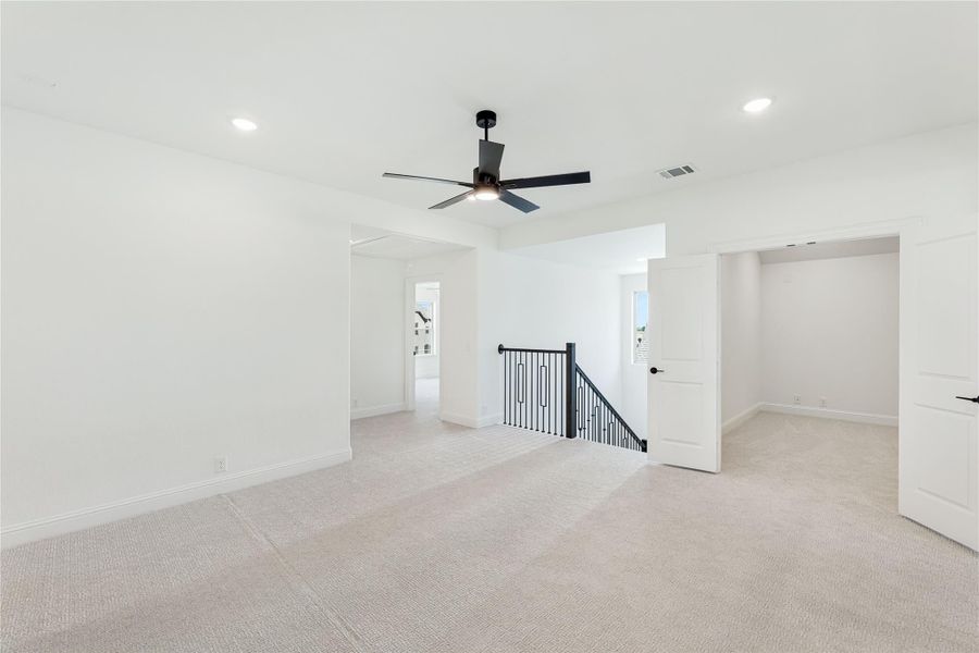 Open upstairs loft with carpet flooring, black ceiling fan, and iron stair railing