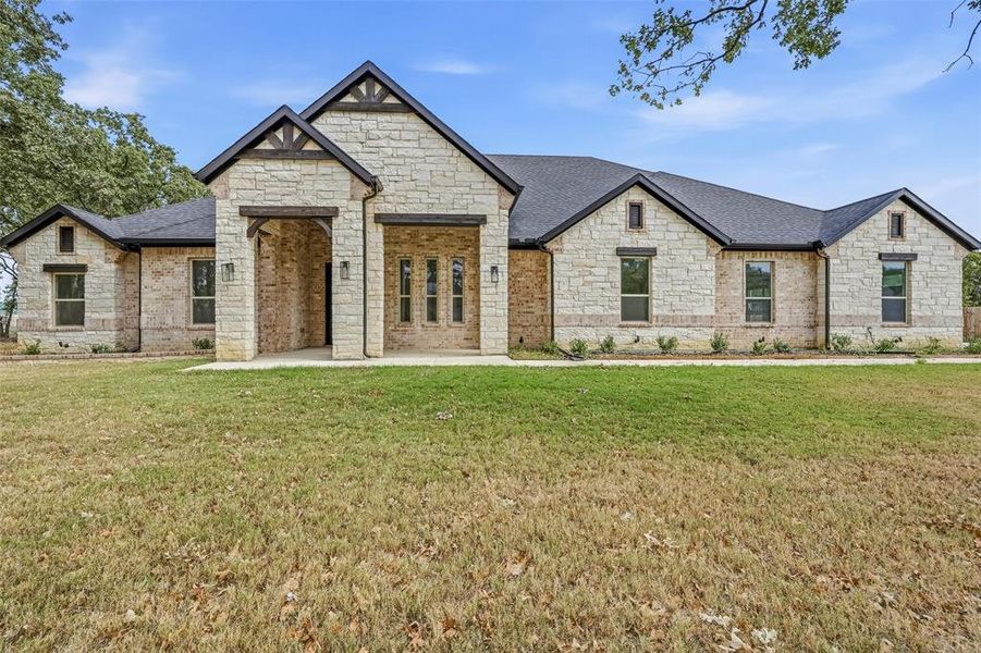 French country style house featuring a shingled roof, brick siding, and stone siding