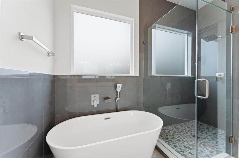 Modern bathroom featuring a sleek freestanding bathtub, glass-enclosed shower with a pebble-tile floor, and a frosted window for privacy.