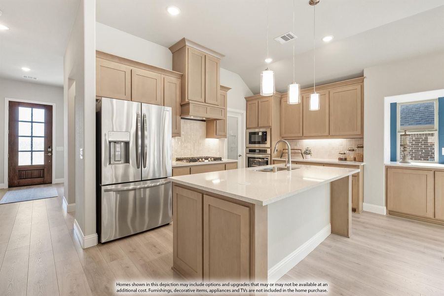 Kitchen with light wood cabinets, center island with sink, stainless steel refrigerator, and pendant lights overhead. Kitchen with light wood cabinets, center island with sink, stainless steel refrigerator, and pendant lights overhead.