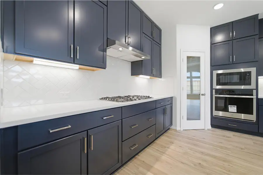 Kitchen with stainless steel appliances, light wood-style floors, light stone counters, tasteful backsplash, and blue cabinetry