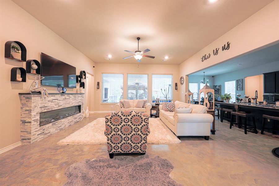 This inviting living room features a modern, open-concept design with a cozy fireplace, neutral tones, and ample natural light from large windows. The space seamlessly connects to a dining area, making it perfect for entertaining.