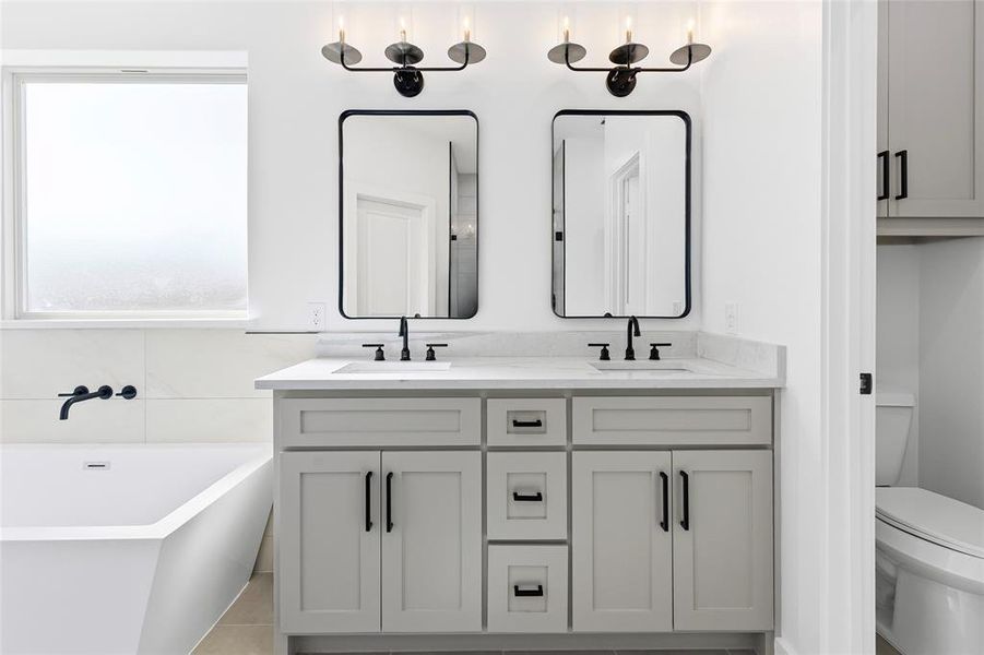 Full bath featuring double vanity, a freestanding tub, toilet, and a sink