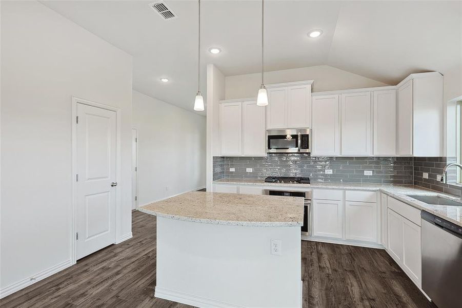 Kitchen with sink, lofted ceiling, white cabinetry, stainless steel appliances, and decorative light fixtures