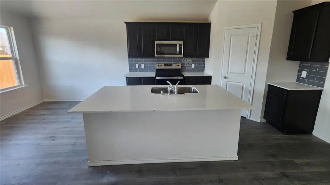 Kitchen featuring a large central island with an undermount sink, dark cabinetry, light countertops, and a subway tile backsplash