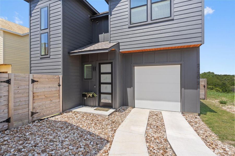 A modern facade with gray siding and large windows, framed by a concrete driveway and natural landscaping. A modern facade with gray siding and large windows, framed by a concrete driveway and natural landscaping.