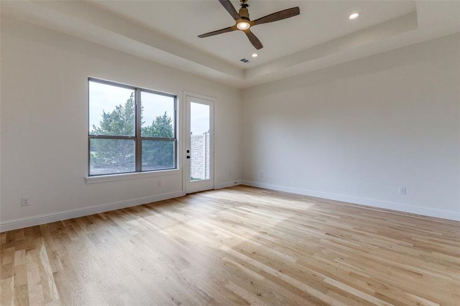 Spare room featuring a tray ceiling, light wood-type flooring, ceiling fan, baseboards, and recessed lighting