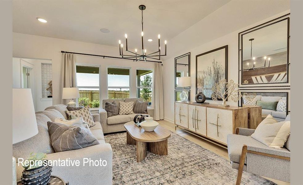 Spacious living area featuring light wood-finish flooring, a contemporary chandelier, multiple large windows, and a built-in wall cabinet with integrated shelving