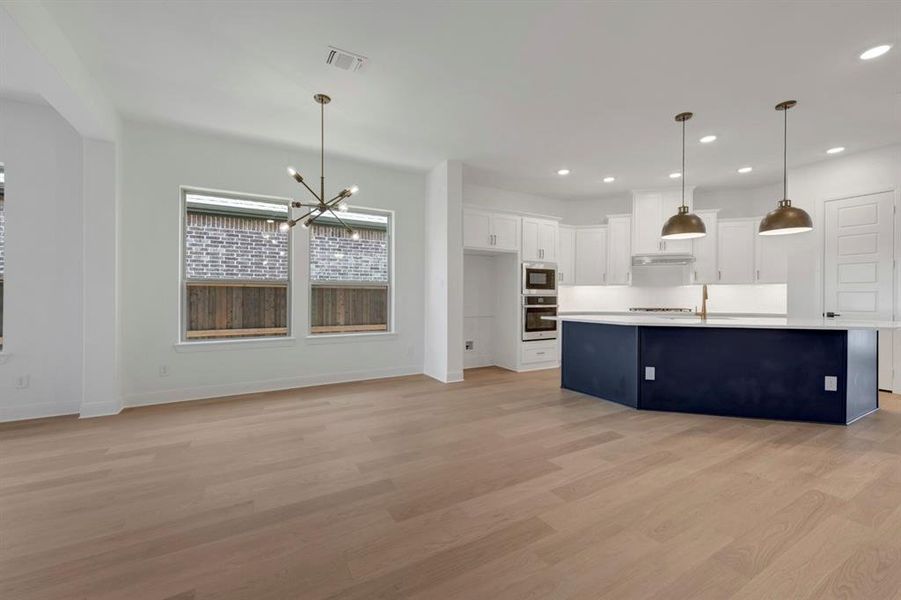 Kitchen featuring a chandelier, light countertops, light wood-style flooring, an island with sink, and two tone color scheme