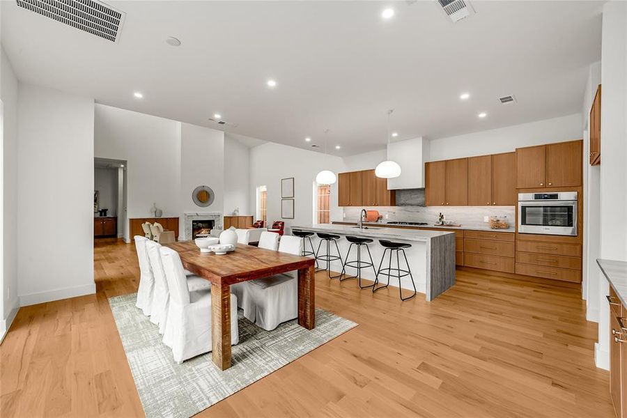 Open-concept living space featuring wood-finish flooring, a kitchen island with seating, a built-in oven, pendant lighting, and a fireplace