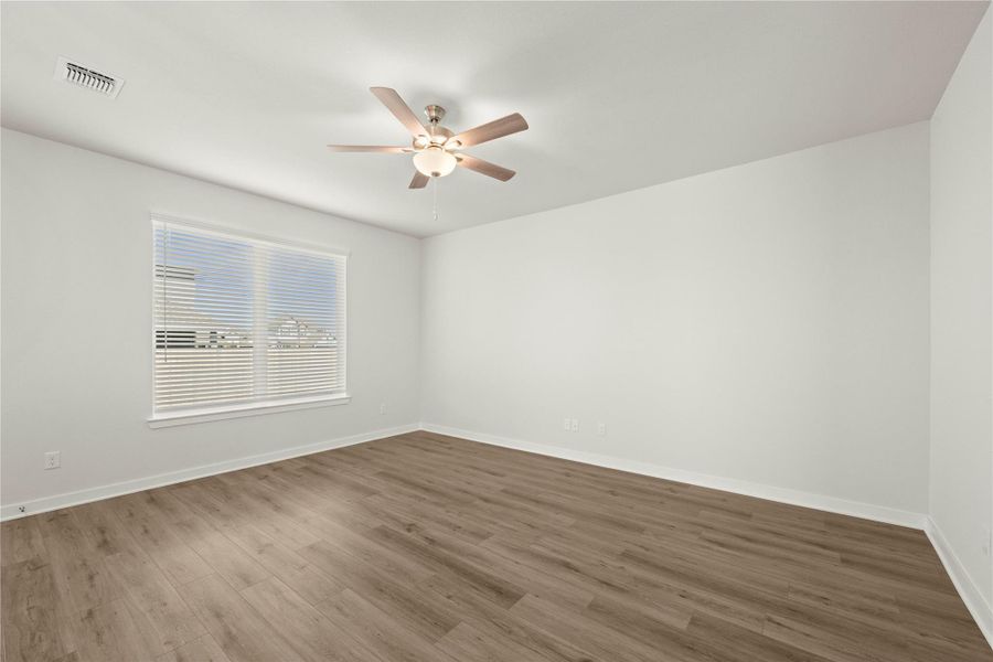 A well-lit bedroom showcasing resilient laminate flooring and a functional ceiling fan.