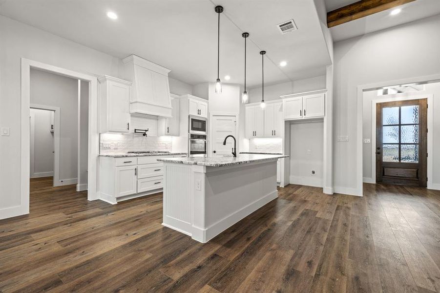 Kitchen with stainless steel appliances, visible vents, white cabinetry, light stone countertops, and a center island with sink