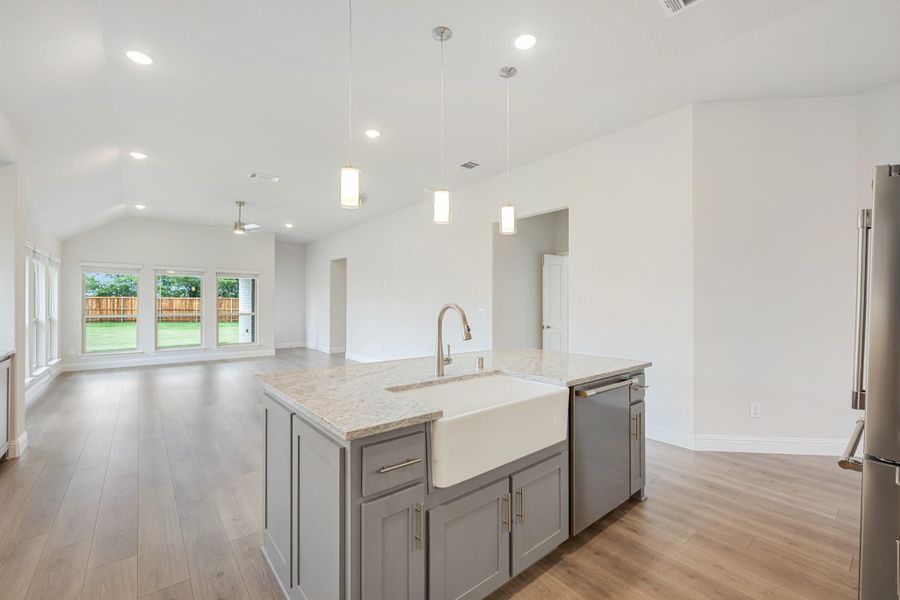 Kitchen island with farmhouse sink, gray cabinets, granite countertop, and pendant lights open to living area Kitchen island with farmhouse sink, gray cabinets, granite countertop, and pendant lights open to living area