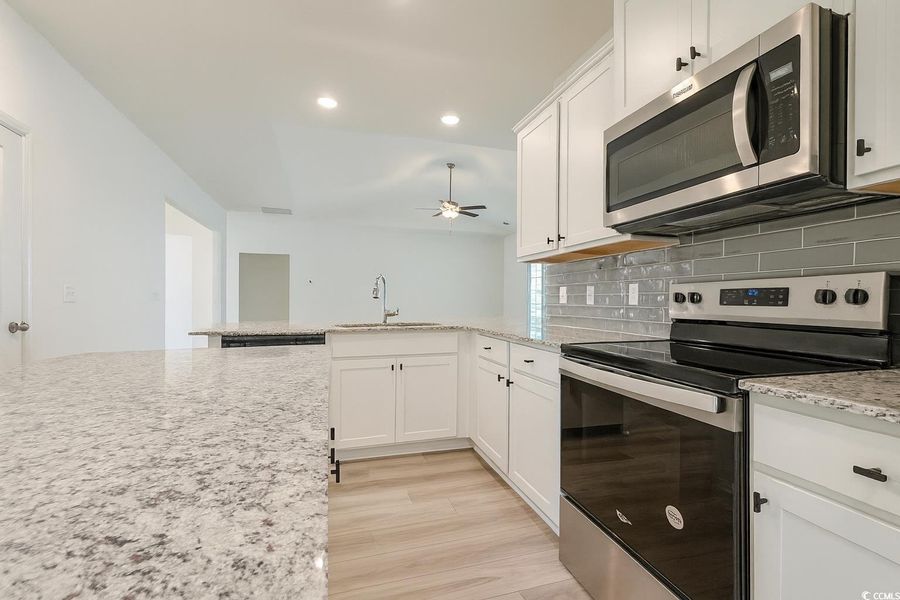 Kitchen with appliances with stainless steel finishes, tasteful backsplash, recessed lighting, white cabinetry, and light stone countertops