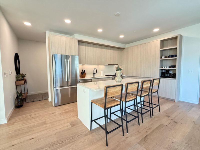 A contemporary kitchen features an island with bar seating and integrated stainless steel appliances.