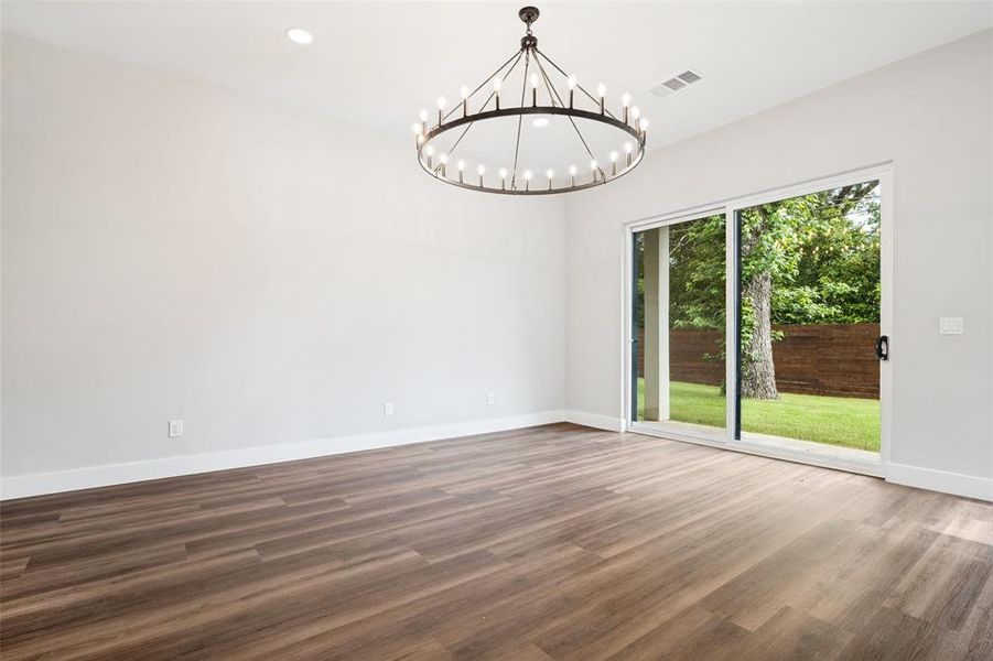 Spacious room featuring wood-finish flooring, a contemporary chandelier, recessed lighting, and a sliding glass door opening to a private backyard with a wood fence