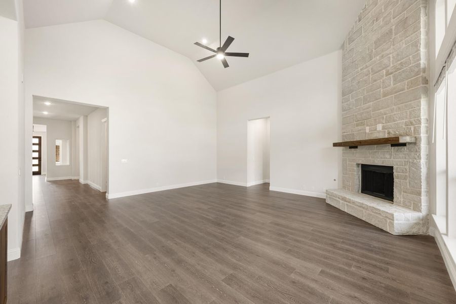 Open living room with vaulted ceiling, stone fireplace, ceiling fan, and dark hardwood floors Open living room with vaulted ceiling, stone fireplace, ceiling fan, and dark hardwood floors