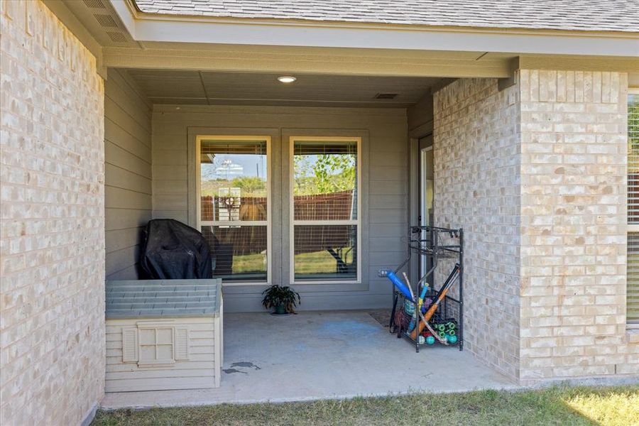 Property entrance with a patio, brick siding, and roof with shingles