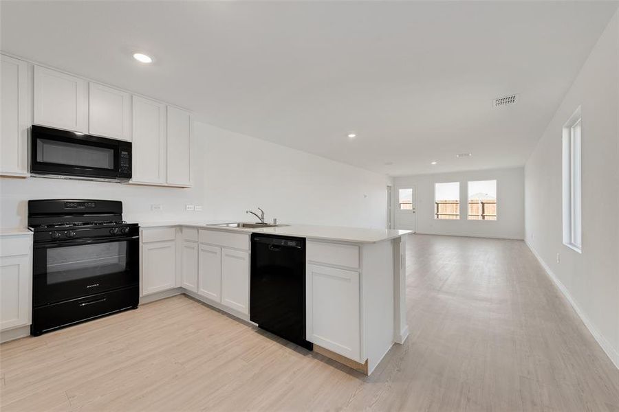 Kitchen with black appliances, light hardwood / wood-style floors, white cabinetry, and kitchen peninsula