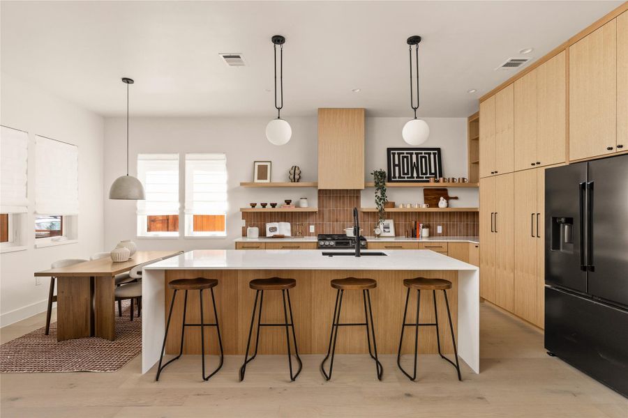 Kitchen with open shelves, pendant lighting, high quality fridge, light stone counters, and light brown cabinets