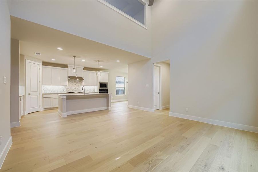 Unfurnished living room featuring light wood-type flooring, recessed lighting, and a towering ceiling Unfurnished living room featuring light wood-type flooring, recessed lighting, and a towering ceiling