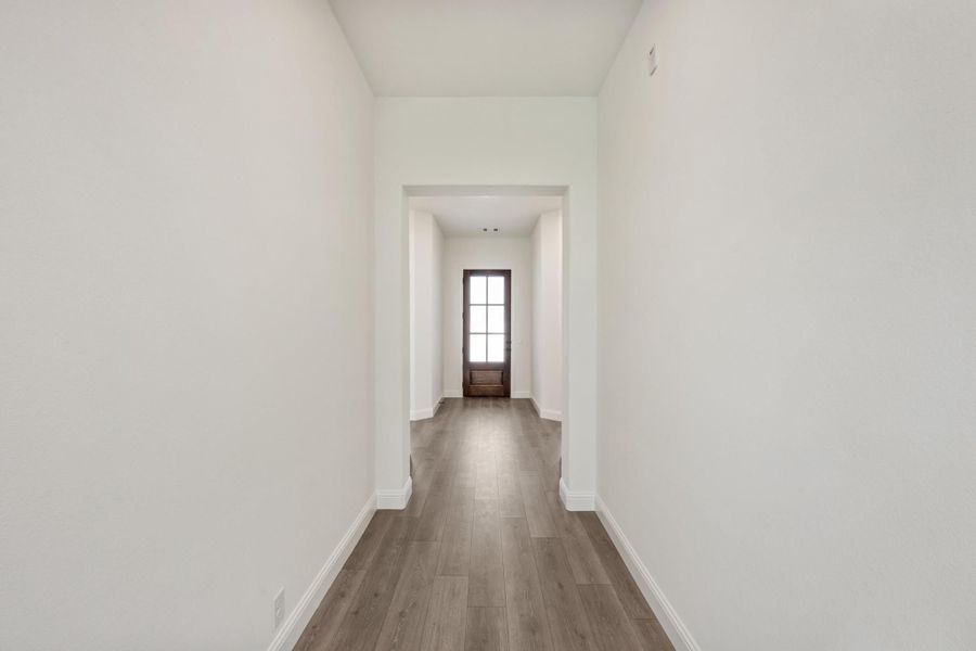 Narrow hallway with white walls, wood-look floors, and a glass-panel front door at the end Narrow hallway with white walls, wood-look floors, and a glass-panel front door at the end
